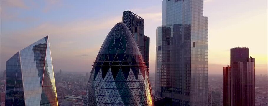 
As the sun begins to set over London, the city's iconic skyline is bathed in a warm, golden glow. From a drone's aerial perspective, the skyscrapers rise majestically, their glass facades reflecting 