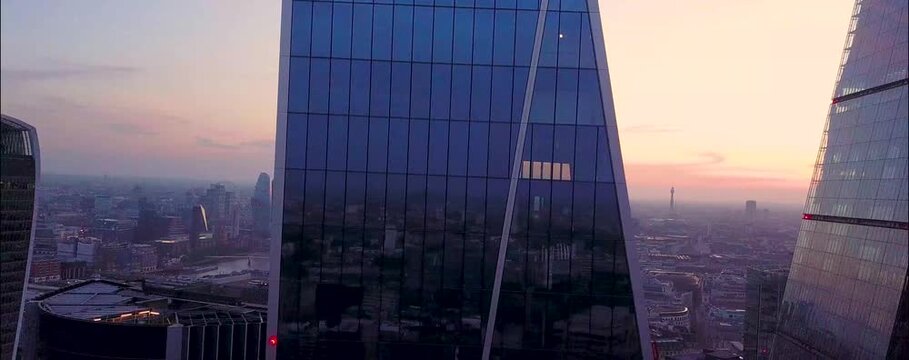 
As the sun begins to set over London, the city's iconic skyline is bathed in a warm, golden glow. From a drone's aerial perspective, the skyscrapers rise majestically, their glass facades reflecting 