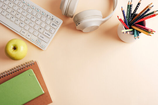 Headphones, keyboard, notepad, pens and apple on neutral beige background. Back to school concept. Top view, flat lay, copy space