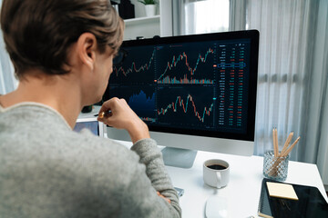 Business trader using computer and laptop to search highest profit value of dynamic increased stock market graph on working desk, analyzing exchange rate value on screen at modern office. Pecuniary.