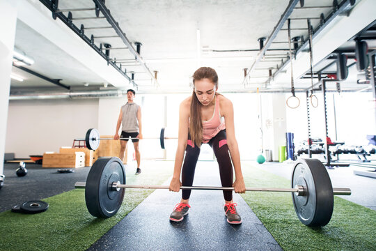 Young fitness girl doing deadlift with barbell in gym, focusing on workout.