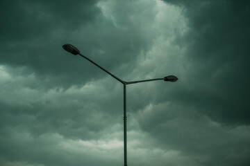 Silhouette of street lamp post against dark stormy clouds in summer