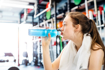 Young fitness girl with dental braces feeling exhausted after hard workout in gym, drinking water.