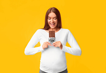 Pregnant Woman Eating Chocolate Standing On Pink Studio Background. Pregnancy Nutrition Concept