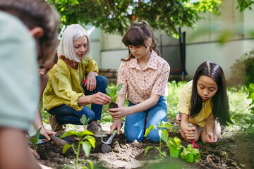 Portrait of students and female teacher at outdoor sustainable education class. Planting vegetable seedling, herbs in soil. Concept of experiential learning and ecoliteracy.