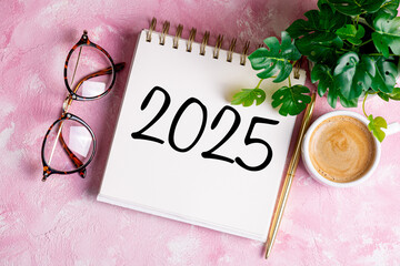 New year resolutions 2025 on desk. 2025 resolutions list with notebook, coffee cup on pink table....