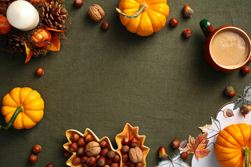 Top view pumpkins, decorative candle, pine cones, nuts, acorns, coffee cup on green cloth on table. Autumn frame. Fall, Thanksgiving concept.