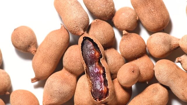 Tamarind tropical fruits background. Heap Fresh ripe dryed Tamarind pods (Tamarindus indica, Indian date), healthy vegan food. Top view, flat lay, rotating, slow motion