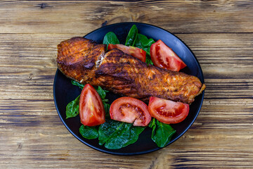 Plate with roasted salmon steak, tomatoes and spinach leaves on a wooden table