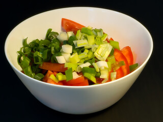 Salad bowl with tomato, cucumber, scallion, spring onion on the black table