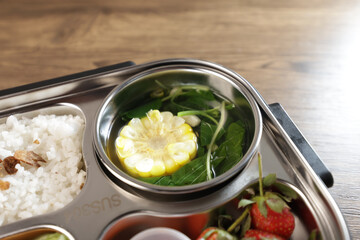 Lunch or bento is put in a lunch box. There are vegetables, side dishes, fruit and also rice.