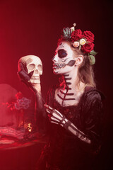 Woman posing with skull in hand, doing Hamlet scene during theatre play while wearing skeleton makeup. Lady dressed for day of the dead spectacle, playing with black rose