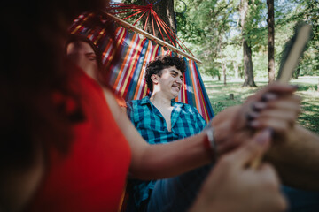 Friends having fun and relaxing together in a colorful hammock on a sunny day in the park, surrounded by trees.
