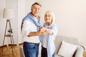 Fototapeta premium Elderly couple dancing together in the living room, smiling to camera