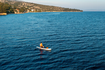 A tourist glides smoothly across the azure sea on a paddleboard or SUP, aerial view