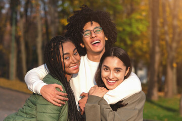 Cheerful african guy hugging his smiling girlfriends over park background