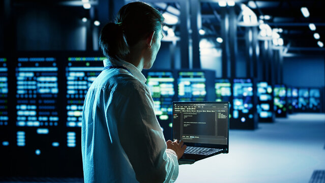 Qualified IT developer running code on laptop, troubleshooting and upgrading data center equipment designed to accommodate server cabinets, networking systems and storage arrays