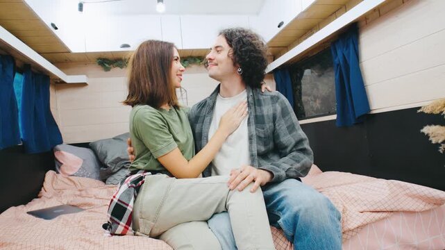 A couple embraces on the bed inside their camper, surrounded by a warm boho atmosphere. The intimate moment highlights their close bond in the cozy, bohemian-styled space