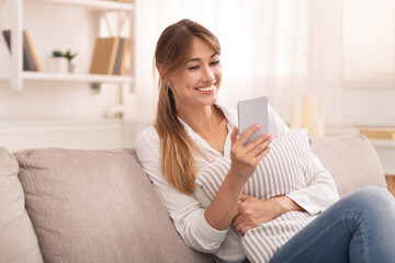 Online Chat. Positive Lady Using Smartphone Texting With Online Friends Relaxing Sitting On Couch At Home