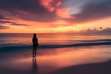 Woman standing on beach watching sunset over ocean horizon, serene scene at dusk