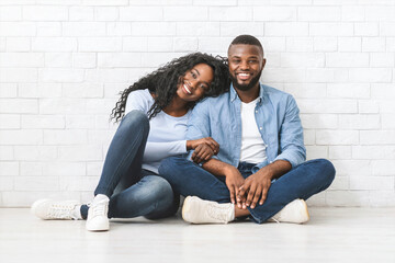 Lovely young african couple sitting on floor at living room and embracing, just moved in, copy space