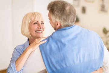 Active mature couple dancing and smiling to each other in living room