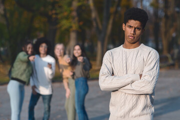 Upset african guy standing over laughing group of international teenagers, bullying concept