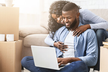 African couple in love checking interior ideas for new apartment using laptop, lady embracing her man, free space