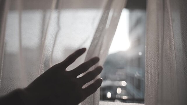 カーテンを開けようとする人の手と太陽の光