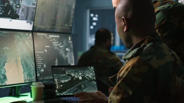 Military soldier in mission control center, overseeing national safety operations using notebook next to colleague. Team of army specialists examining data in monitoring room command center, camera A