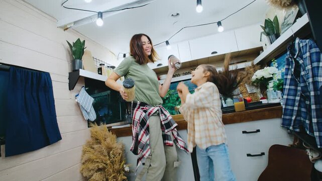 A girl and her daughter joyfully dance in their cozy camper kitchen, embracing the warm, boho atmosphere inside.