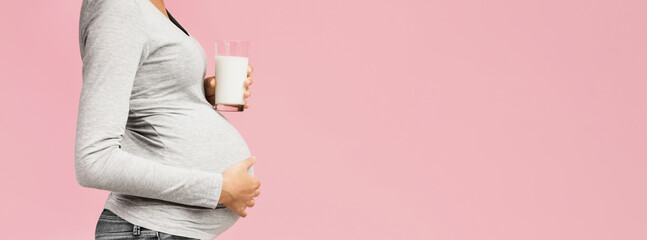 Healthy diet during pregnancy. Lady holding glass of milk, pink background with copy space, side...