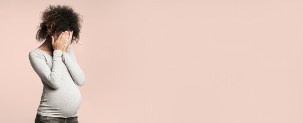 Depression during pregnancy. Afro woman covering face with hands and crying, grey background