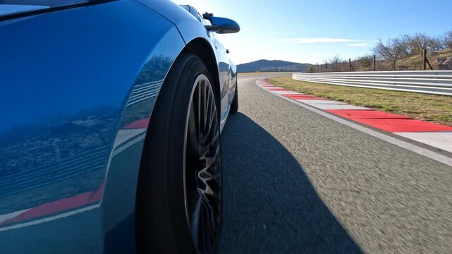 LOW ANGLE, CLOSE UP: Metallic blue sports car racing on a closed circuit during a track day sparkles in the bright autumn sunshine. Cool wheel shot of a sportscar speeding down racetrack during race.
