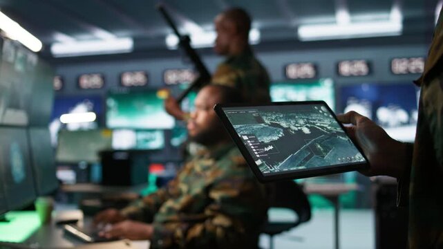 Military agent working in control room, using software on tablet, analyzing aerial reconnaissance data. Close up of intelligence corps expert controlling drones with portable device, camera B