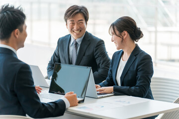 企業のオフィスで笑顔で会議・ミーティング・商談をするビジネスマン・ビジネスウーマン
