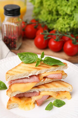 Pieces of toasted bread with melted cheese, ham and basil on table