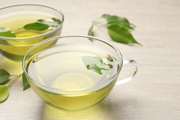 Refreshing green tea in cups and leaves on wooden table, closeup