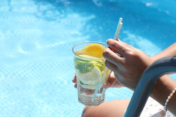 Woman holding tasty cocktail in glass near swimming pool outdoors, closeup