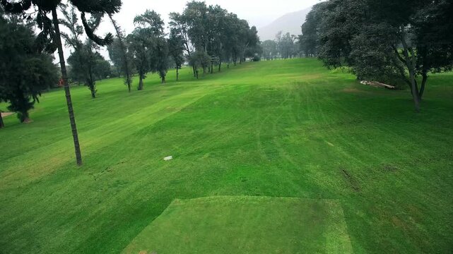  dynamic aerial shot captured by a drone, showcasing a golf tee-off area and the initial stretch of the fairway. The image highlights the meticulously maintained green, with the tee box , Drone view, 