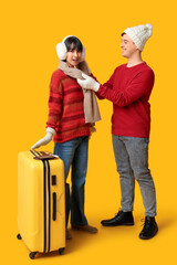 Beautiful young happy couple with suitcase, passports and tickets on yellow background. Winter vacation concept