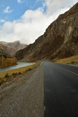 A new asphalt road running at the foot of a high cliff along the bank of a beautiful winding river under an autumn cloudy sky in the shade.