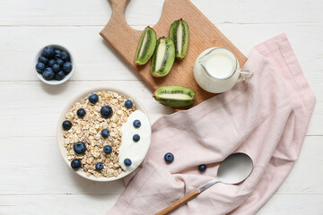 Napkin, wooden board, kiwi, bowl with raw oatmeal and berries on white wooden background