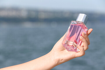 Female hand with bottle of perfume near river, closeup