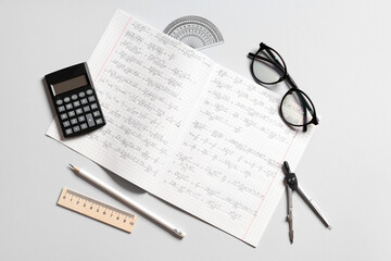 Copybook with handwritten maths formulas, eyeglasses and stationery on grey background