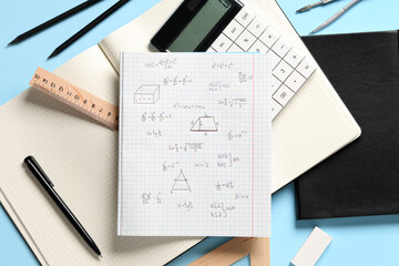 Copybook with handwritten maths formulas and stationery on blue background