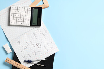 Copybook with handwritten maths formulas and stationery on blue background