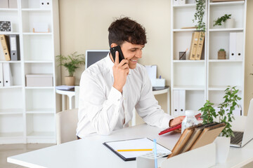 Fototapeta premium Male accountant talking on mobile phone and holding calculator at workplace in office