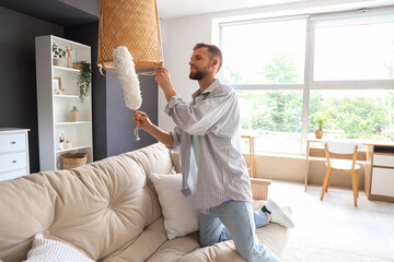 Male janitor cleaning lamp with dust brush on in room