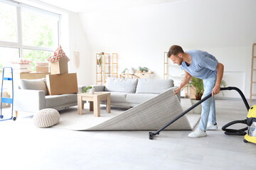 Male janitor cleaning floor under carpet with vacuum cleaner in room